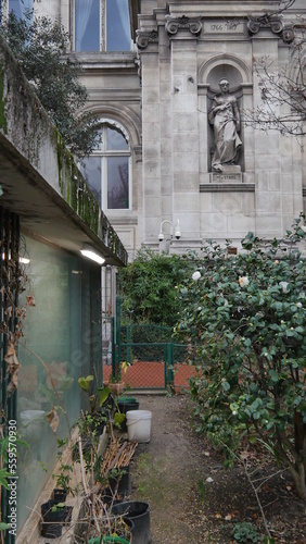 Un petit coin de jardinage ou de parc public, avec un chemin en gravier, des buissons bien taillés, une fine d'arbre sans feuilles et un batiment historique et ancien