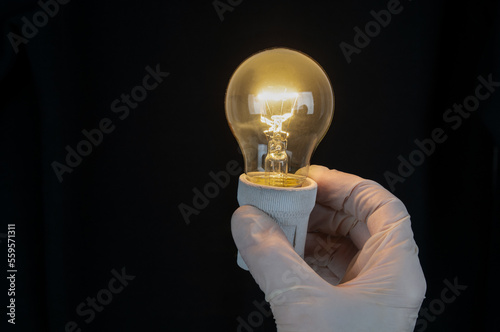Hand in glove holding old vintage light bulb on black background