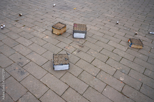 Tattered fireworks and the remains of fireworks  lie on the sidewalk.