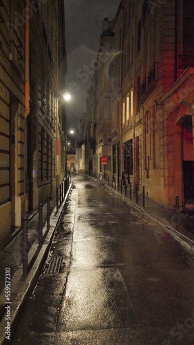 Sombre rue plongée dans la nuit, éclairé par des lampadaires nocturnes, mystérieux, obscur, peu de passant, passage de pluie, sol mouillé