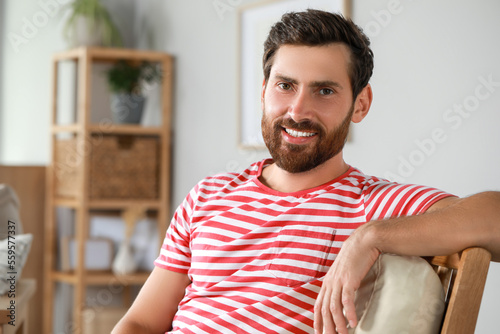 Portrait of handsome bearded man in armchair at home, space for text