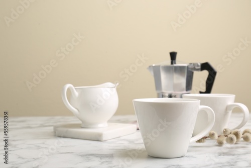 Cups, moka pot and jug on white marble table. Space for text