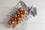 Fresh raw chicken eggs and whisk on white wooden table, flat lay