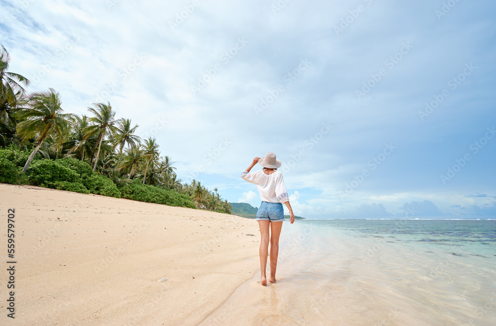 Vacation on the seashore. Back view of young woman walking away on the beautiful tropical white sand beach. Vacation on the seashore. Back view of young woman walking away on the beautiful tropical white sand beach.