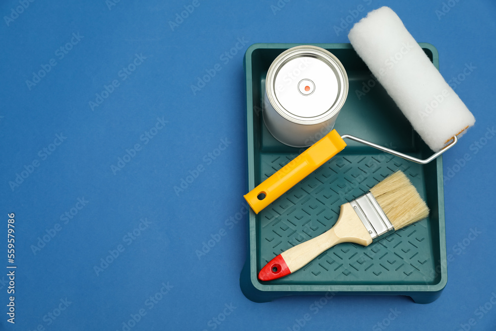 Can of orange paint, brush, roller and container on blue background, flat lay. Space for text