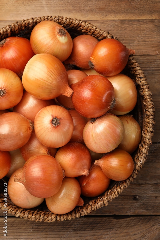 Wicker basket with many ripe onions on wooden table, top view Wicker basket with many ripe onions on wooden table, top view