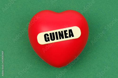 On a green surface lies a red heart with the inscription - Guinea