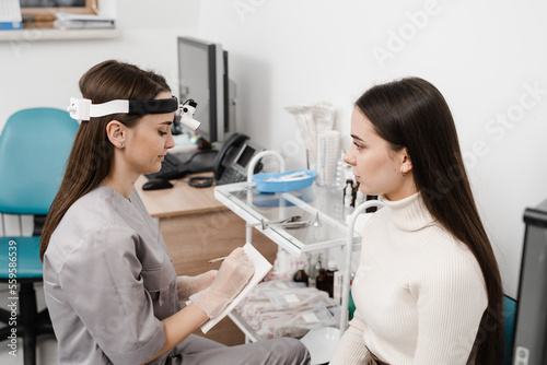 Fototapeta Naklejka Na Ścianę i Meble -  ENT doctor consulting patient and write notes causes of difficulty breathing. Consultation of woman with otolaryngologist in a medical clinic.