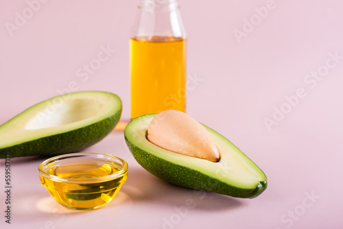 Avocado oil in a bowl and avocado halves on a pink background. Home beauty care.