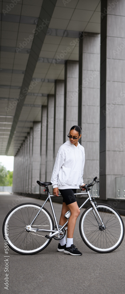 Vertical banner of african american woman looking at bicycle on street Vertical banner of african american woman looking at bicycle on street
