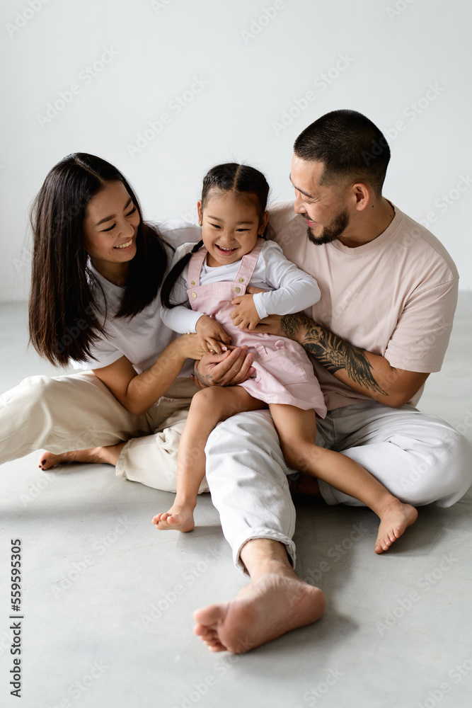 Young barefoot asian family with daughter playing while sitting on grey background