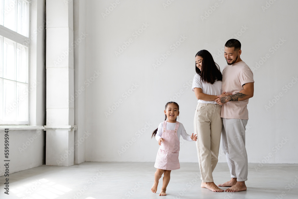 Cheerful toddler asian child running near happy young parents on grey background Cheerful toddler asian child running near happy young parents on grey background