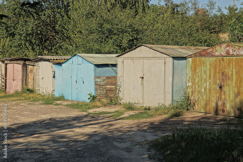 Old colored iron garages in the thickets of grass near the road in the street