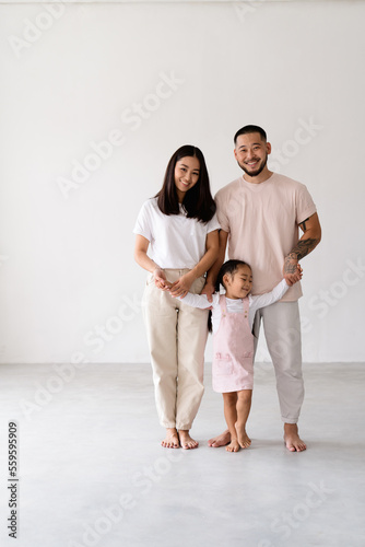 Smiling modern asian family with toddler daughter looking at camera on grey background