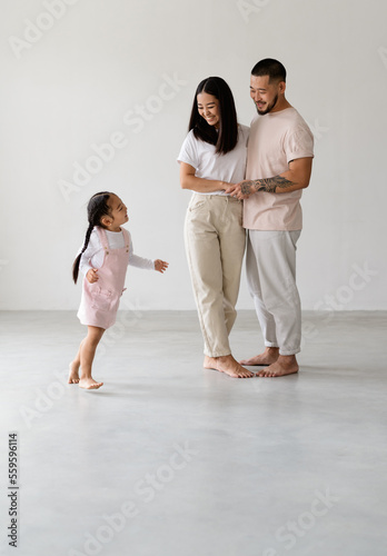 Cheerful barefoot asian child running near young modern parents on grey background