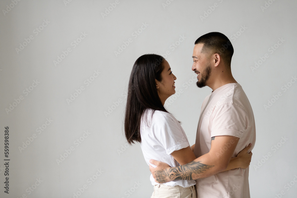 Profile of smiling asian couple hugging and looking at each other isolated on grey background Profile of smiling asian couple hugging and looking at each other isolated on grey background