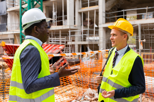 Two civil engineers working at the construction site communicate, discussing current work issues