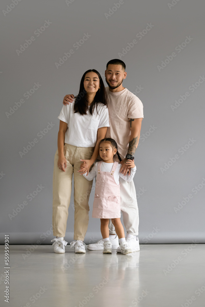 Smiling and stylish asian family with baby daughter standing on grey background Smiling and stylish asian family with baby daughter standing on grey background