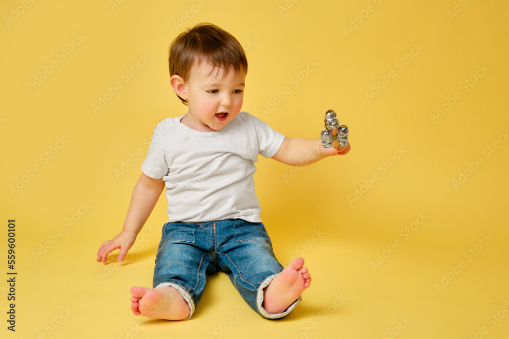 Toddler baby plays with a musical rattle bells on a stick, studio yellow background. Happy child musician playing percussion musical instrument, copy space. Kid aged one year and four months Toddler baby plays with a musical rattle bells on a stick, studio yellow background. Happy child musician playing percussion musical instrument, copy space. Kid aged one year and four months