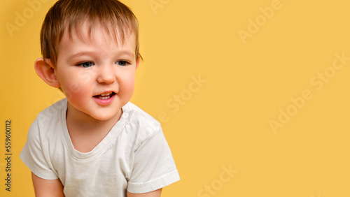 Portrait of a happy toddler baby on a studio yellow background. Smiling child in a white t-shirt, copy space. Kid aged one year and four months