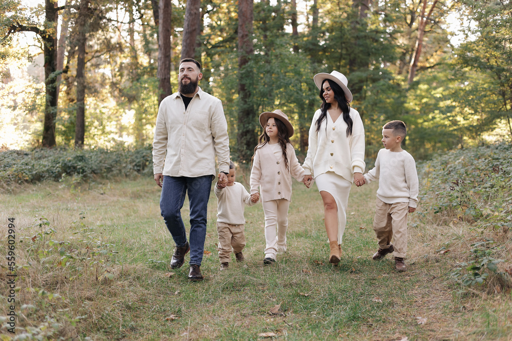 Young mother, father with daughter and sons are walking, having fun in autumn forest. Family holding hands enjoying time together at background of trees. Happy parenthood and childhood concept. Young mother, father with daughter and sons are walking, having fun in autumn forest. Family holding hands enjoying time together at background of trees. Happy parenthood and childhood concept.