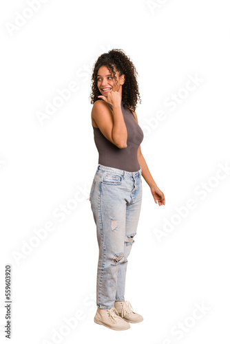 Young african american woman with curly hair cut out isolated points with thumb finger away, laughing and carefree.