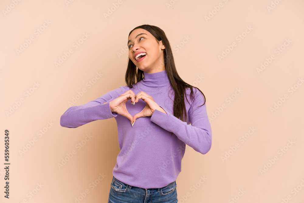 Young colombian woman isolated on beige background smiling and showing a heart shape with hands. Young colombian woman isolated on beige background smiling and showing a heart shape with hands.
