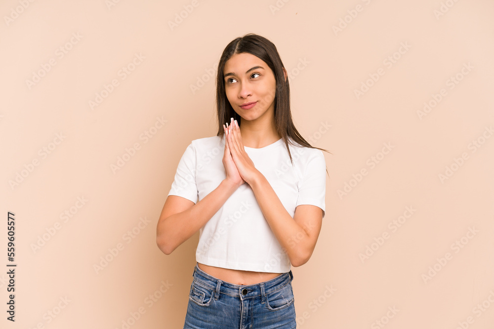 Young colombian woman isolated on beige background praying, showing devotion, religious person looking for divine inspiration. Young colombian woman isolated on beige background praying, showing devotion, religious person looking for divine inspiration.