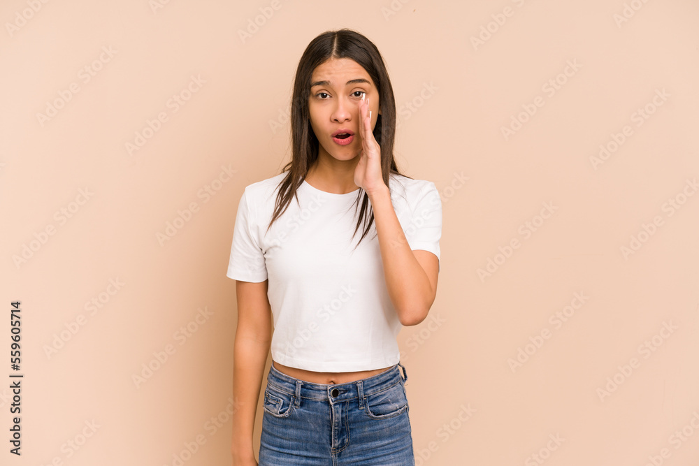 Young colombian woman isolated on beige background is saying a secret hot braking news and looking aside