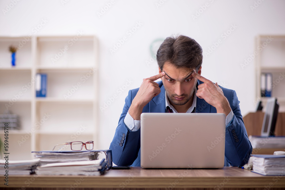 Young male employee unhappy with excessive work in the office Young male employee unhappy with excessive work in the office