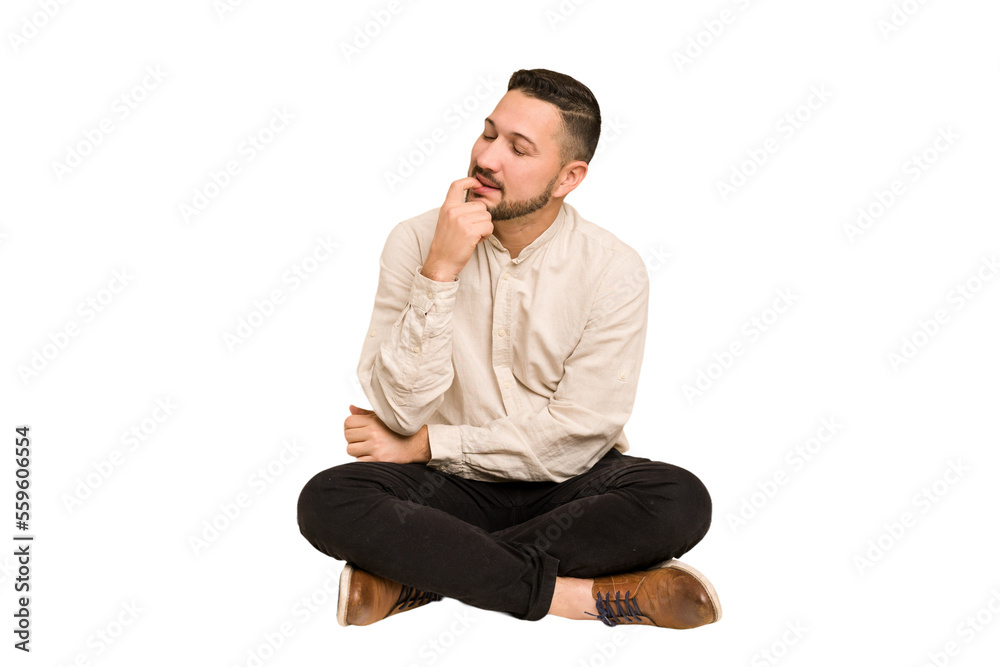 Adult latin man sitting on the floor cut out isolated relaxed thinking about something looking at a copy space. Adult latin man sitting on the floor cut out isolated relaxed thinking about something looking at a copy space.