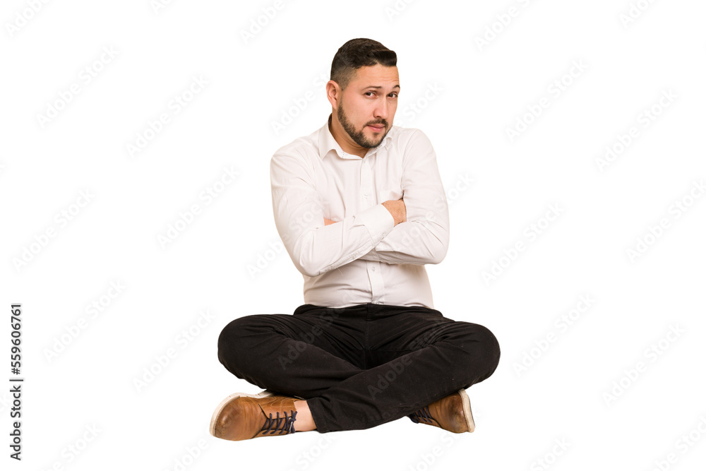 Adult latin man sitting on the floor cut out isolated suspicious, uncertain, examining you. Adult latin man sitting on the floor cut out isolated suspicious, uncertain, examining you.
