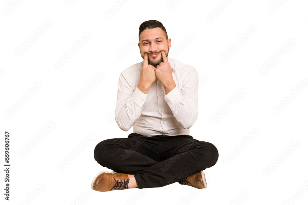 Adult latin man sitting on the floor cut out isolated doubting between two options.