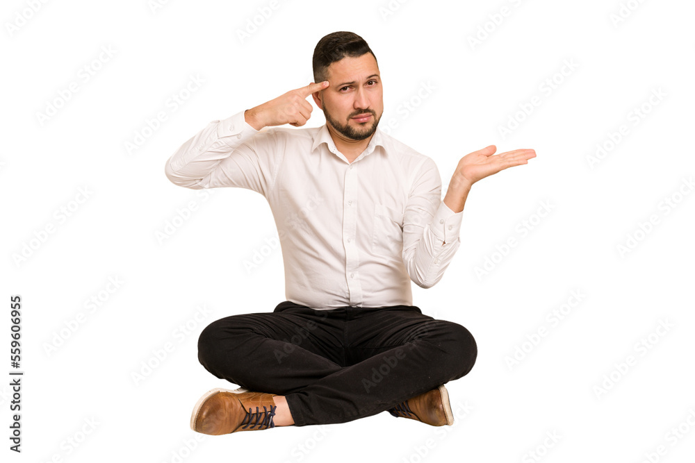 Adult latin man sitting on the floor cut out isolated holding and showing a product on hand. Adult latin man sitting on the floor cut out isolated holding and showing a product on hand.