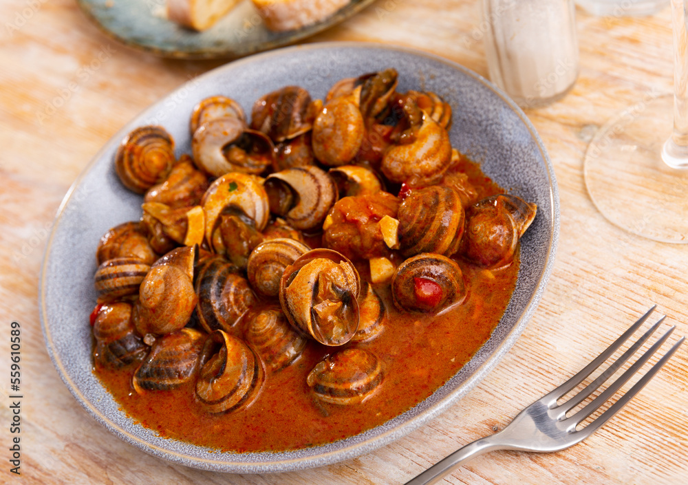 Fototapeta premium Andalusian style appetizer of land snails caracoles stewed with salsa of tomatoes, garlic, rosemary, hot peppers and olive oil. Traditional Spanish cuisine