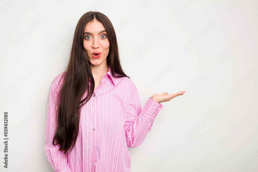 Young caucasian woman isolated on white background impressed holding copy space on palm.