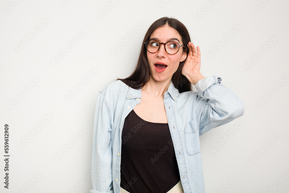 Young caucasian woman isolated on white background trying to listening a gossip.