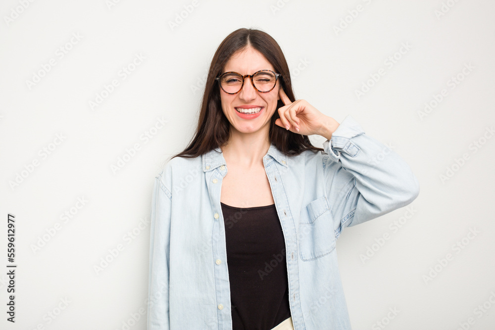 Young caucasian woman isolated on white background covering ears with hands.