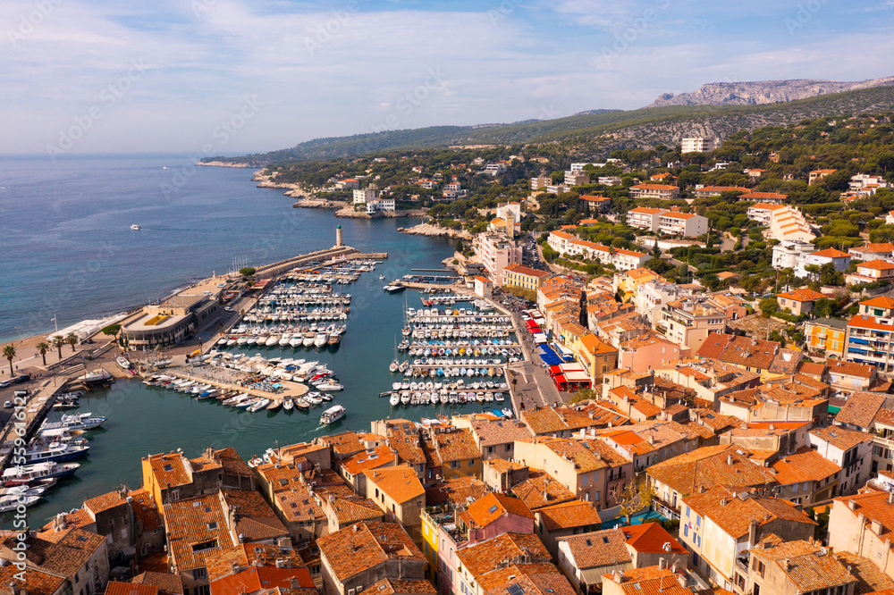 Scenic drone view of coastal small French town of Cassis overlooking port with moored yachts on sunny day .