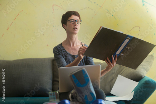 Woman with broken leg working on laptop and reading document photo