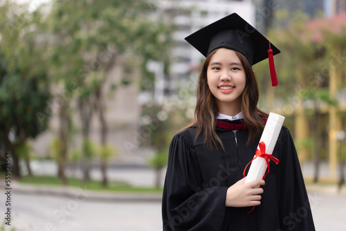 Successful graduation from university. Smiling beautiful Asian girl university or college graduate standing with diploma over university at background.