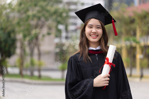 Successful graduation from university. Smiling beautiful Asian girl university or college graduate standing with diploma over university at background.