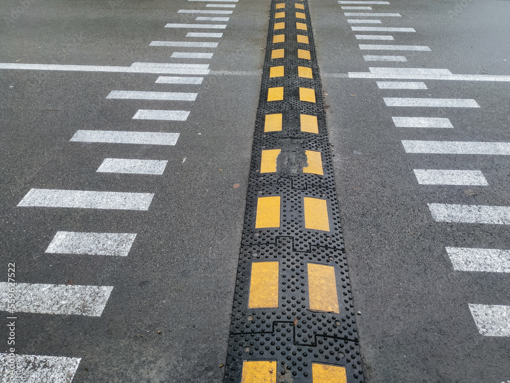 Rubber speed bump on asphalt with road markings of a pedestrian crossing.