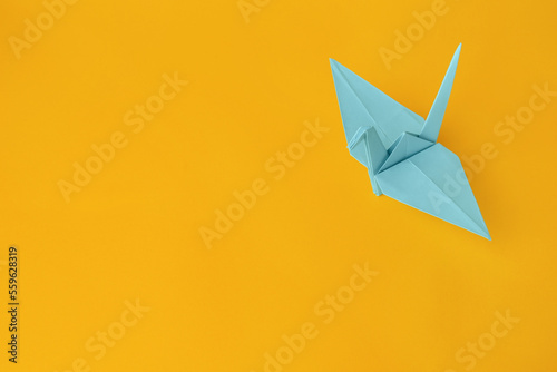 Origami art. Beautiful light blue paper crane on orange background  space for text