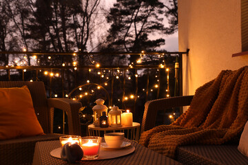 Beautiful view of garden furniture with pillow, soft blanket and burning candles at balcony