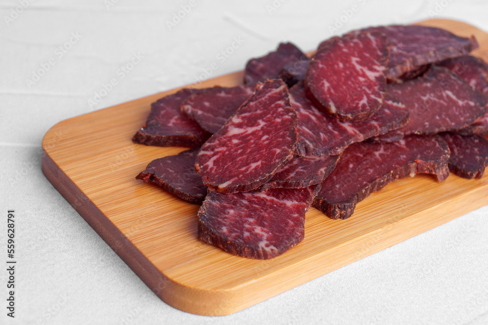 Pieces of delicious beef jerky on white textured table, closeup