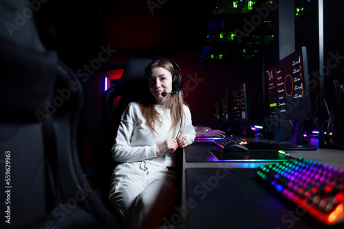 girl gamer sits in headphones in a computer club looks at the camera and smiles, portrait of a cybersports girl