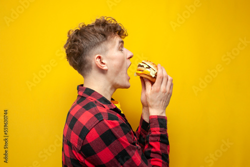 curly guy student eats a burger on a yellow background, a man with fast food