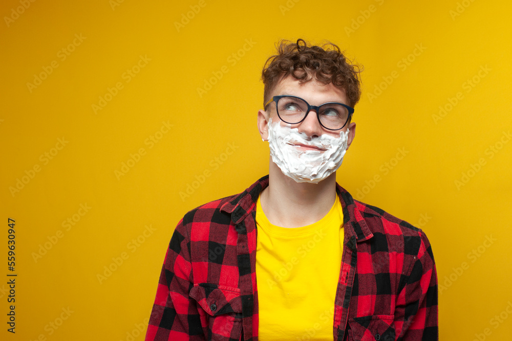 curly guy with shaving foam on his face dreams and thinks on, student shaves his beard and looks up at copy space curly guy with shaving foam on his face dreams and thinks on, student shaves his beard and looks up at copy space
