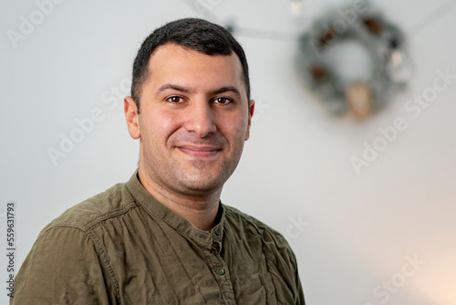 An emotional portrait of a middle-aged man against the background of a Christmas wreath and a light background.